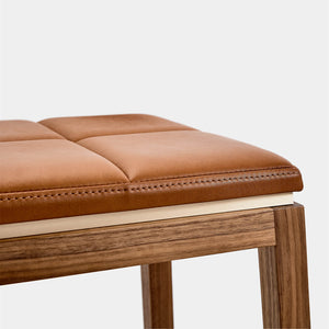 A zoomed in view of the metal shadowline detailing gliding between the supple leather seat and solid wood frame of a designer stool