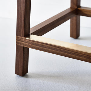 grand brass metal detail footrest close up of a solid wood stool resting on a concrete floor 