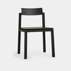 a modern black wood dining chair faces side on revealing its curved back
