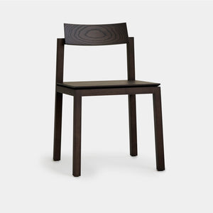 A perspective angle reveals a solid wood modern dining chair stained in an earth colour